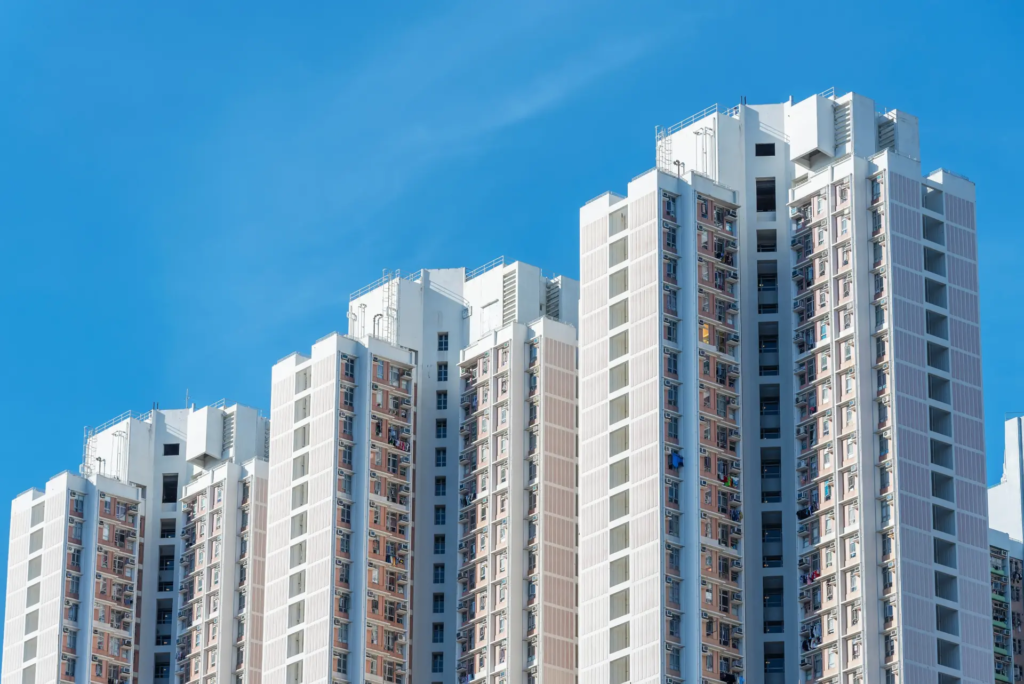 Vue en plongée d'un complexe d'immeubles résidentiels modernes et hauts sous un ciel bleu clair. Les bâtiments présentent une architecture répétitive avec de nombreux balcons et fenêtres.