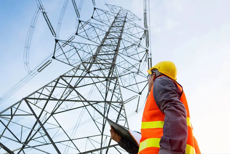 Un homme en tenue de chantier regarde en l'air vers un pilonne électrique