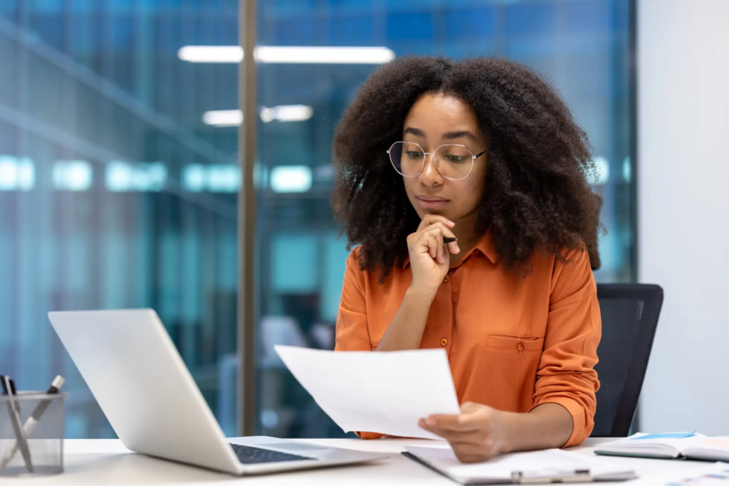 Femme lisant un document papier, assise dans un bureau vitré