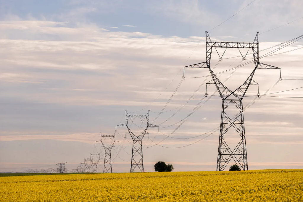 Lignes électriques à haute tension traversant un champ sous un ciel nuageux