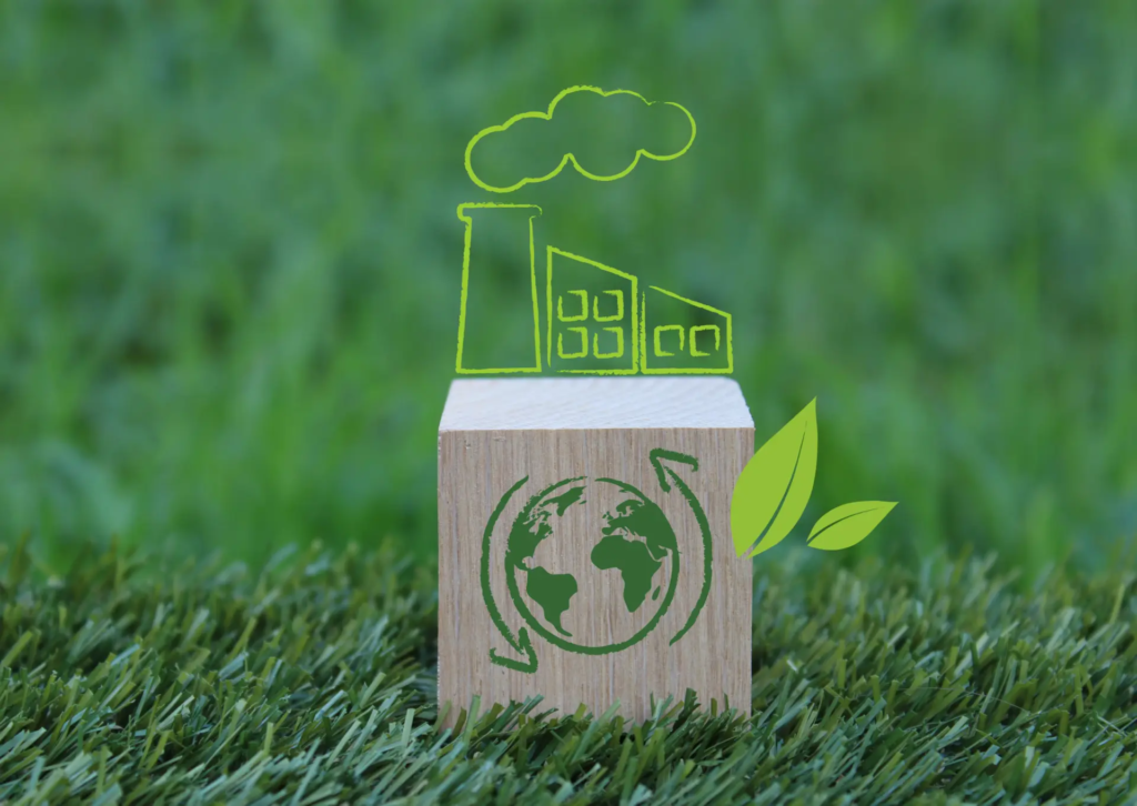 Cube en bois posé sur l’herbe avec la planète dessinée dessus et, au-dessus, un pictogramme d’usine fumante, symbolisant les enjeux de la transition énergétique des entreprises.