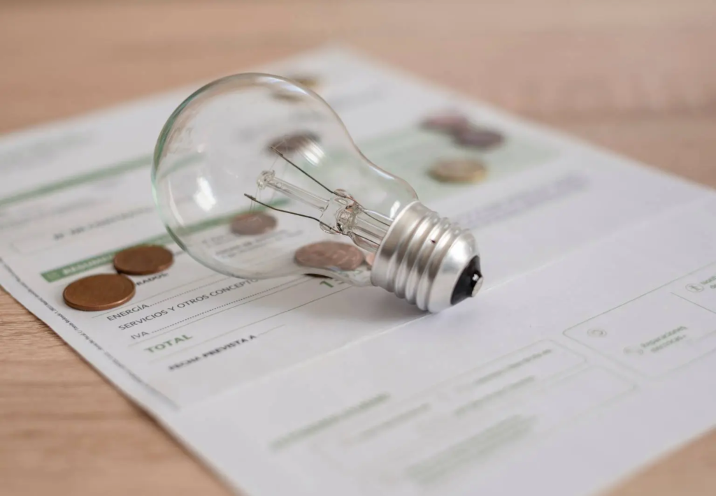 Ampoule posée sur une facture d’électricité avec des pièces de monnaie symbolisant le coût de l’énergie