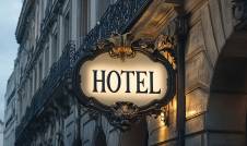 Énergie hôtel restaurant : enseigne lumineuse “HOTEL” sur un immeuble haussmannien avec balustrades en fer forgé.