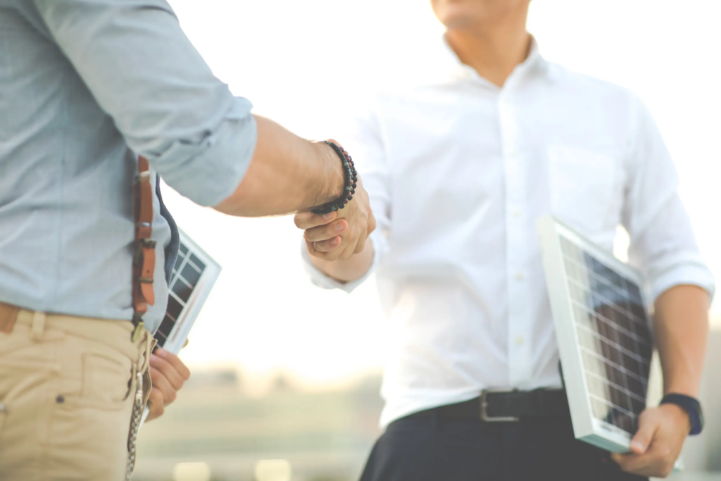 Poignée de main entre deux professionnels concluant un accord, l'un tenant un panneau solaire, illustrant le choix d'un fournisseur d'électricité pour une entreprise.